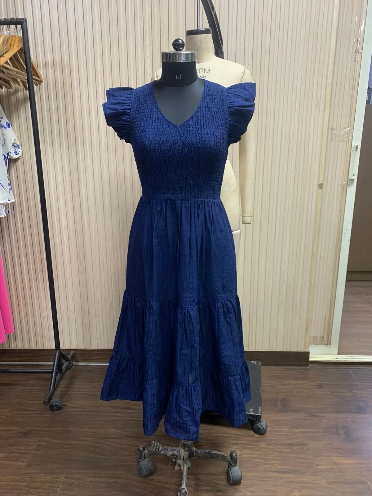 Front view of a navy smocked flutter-sleeve tiered maxi dress on a dress form