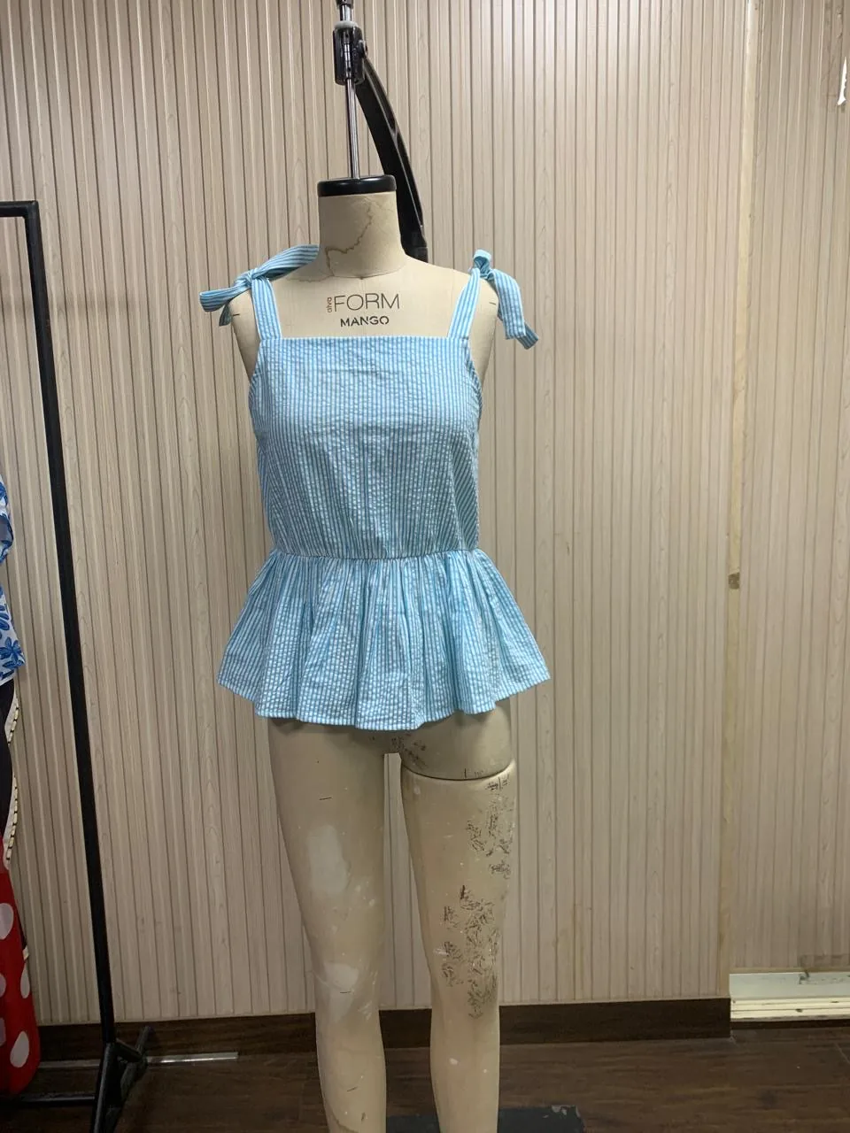 Front view of a light blue tie-shoulder seersucker peplum top on a dress form